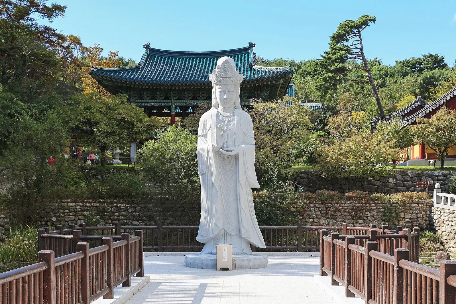연못 위에 서 있는 하얀 보살상과 뒤편 전각