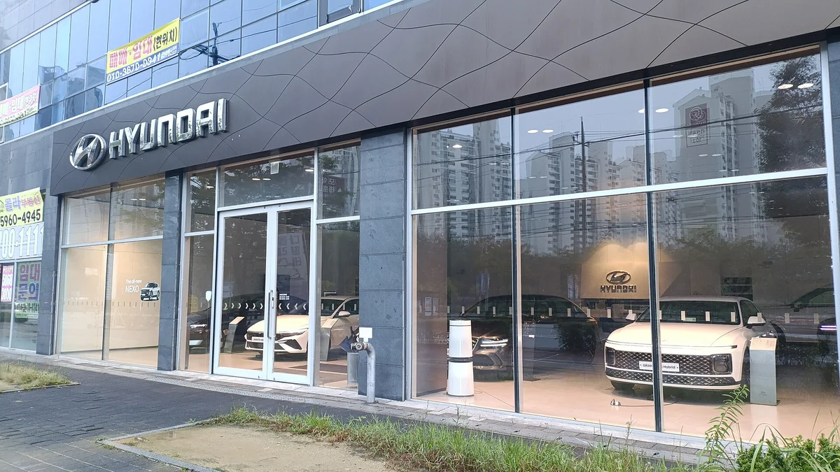 유리 외벽 너머로 흰색 신차가 전시된 현대자동차 전시장의 외관