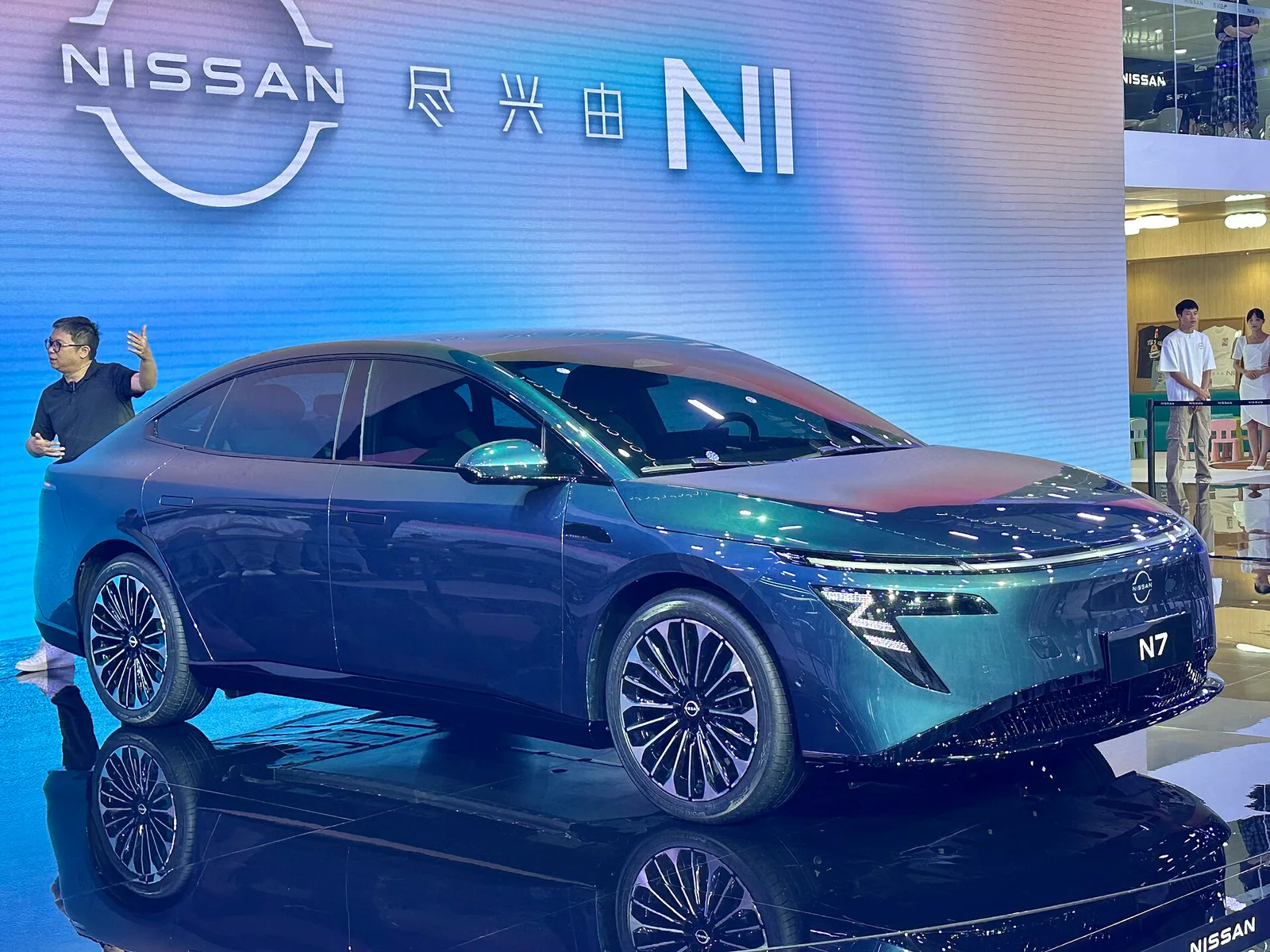 다른 중국 모터쇼 전시장에서 공개된 진회색 닛산 N7의 측면 및 앞모습, 배경에 NISSAN 로고와 중국어 문구가 적힌 조명 패널이 보이는 모습