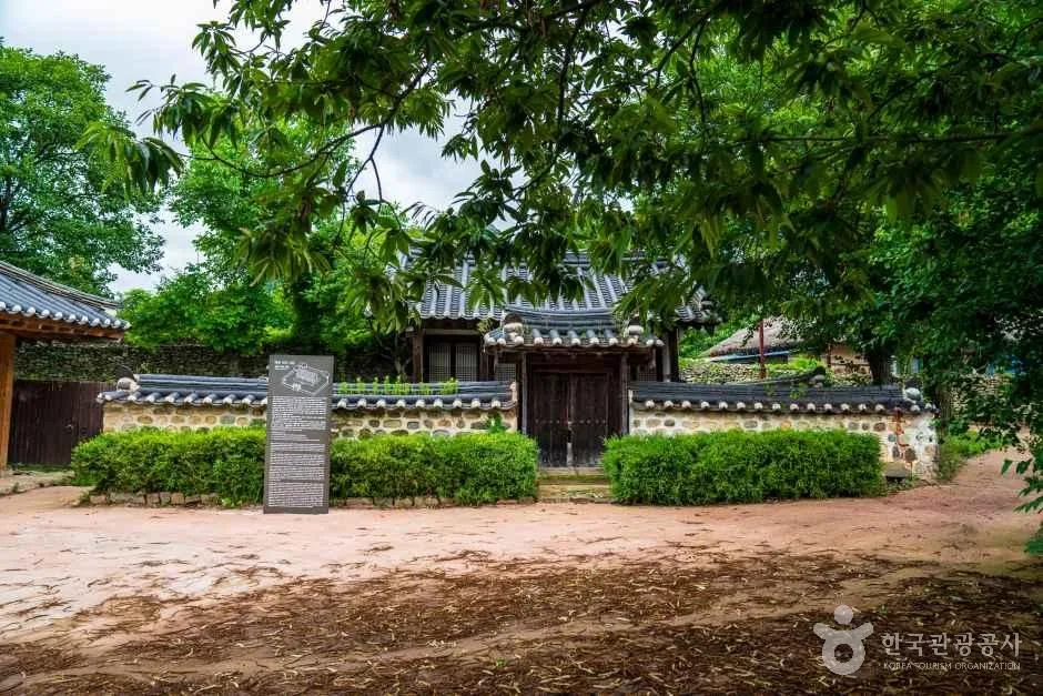 돌담 앞에 안내석이 서 있고 기와 고택이 보이는 흙길