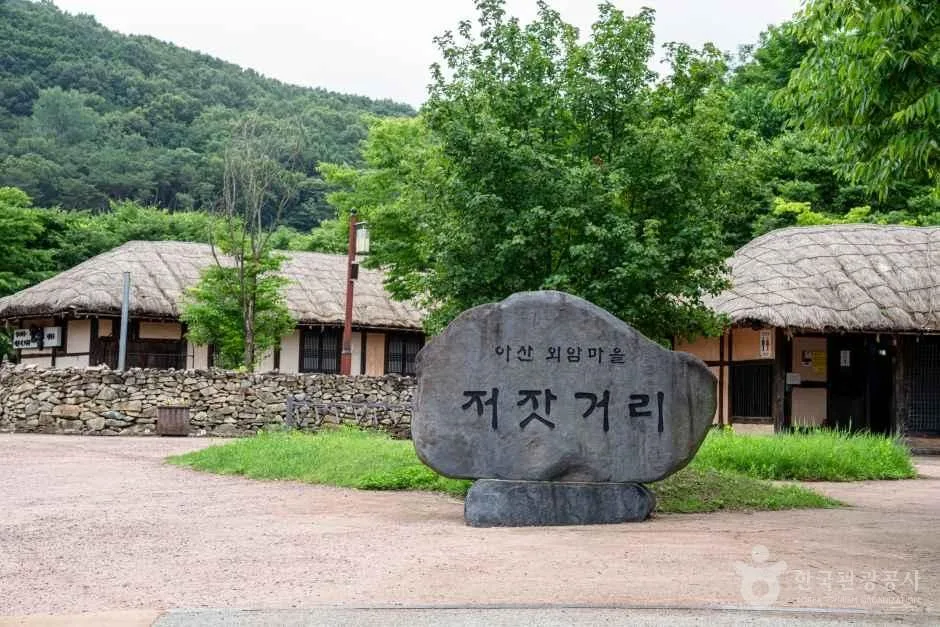 저잣거리라고 새겨진 바위 표지석 뒤로 초가지붕 건물이 늘어선 모습
