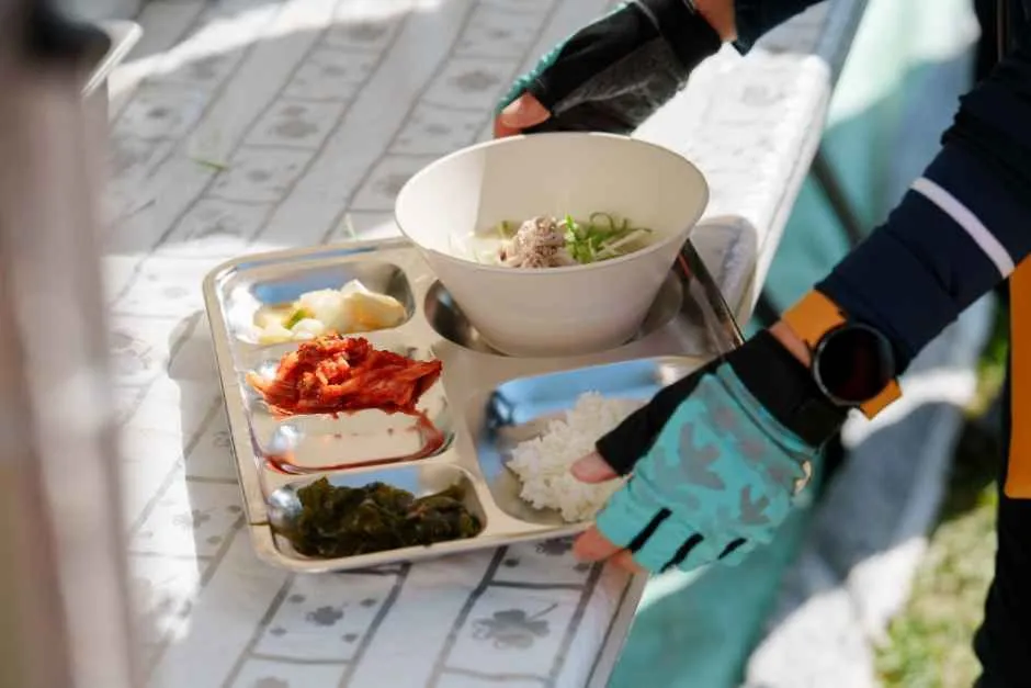 식판에 담긴 죽과 반찬, 걷는 참가자의 장갑 낀 손