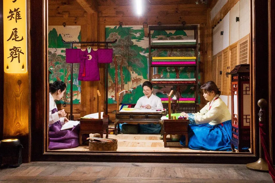 전각 안에서 한복 차림 사람들이 책상 앞에 앉아 작업하는 모습을 유리 너머로 볼 수 있는 재현 장면
