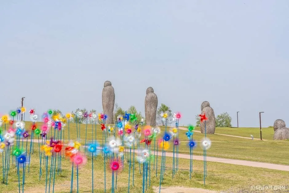 잔디 언덕 위에 색색의 바람개비가 줄지어 서 있고 뒤로 조형물이 보이는 평화누리공원