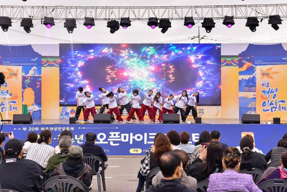축제 무대 위에서 공연팀이 춤을 추고 관객이 앉아 지켜보는 모습
