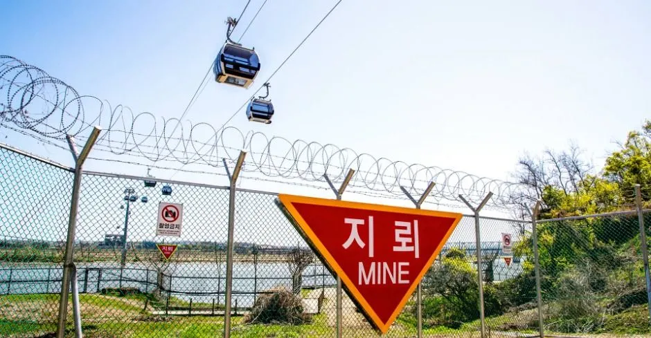 철책 위로 곤돌라 캐빈이 지나가고 지뢰 주의 표지판이 붙어 있는 모습