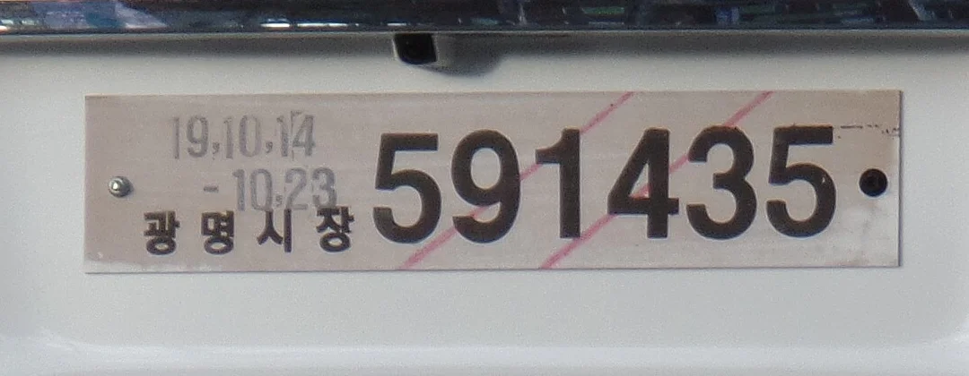 흰색 승용차 뒤쪽에 달린 목재 임시운행허가번호판, 광명시장 발행과 허가기간이 적혀 있고 적색 사선이 그어져 있다