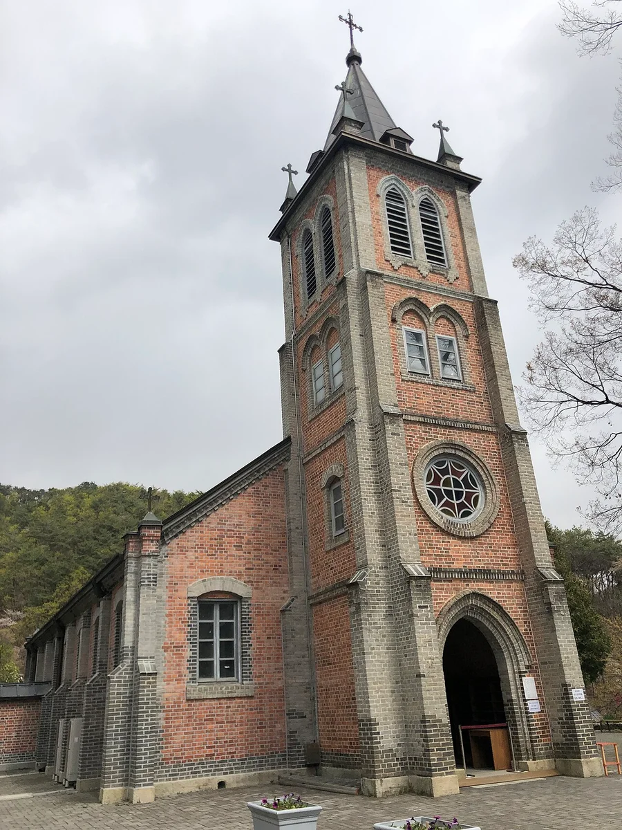 종탑과 붉은 벽돌 측면 벽이 보이는 풍수원성당을 낮은 각도에서 본 사진