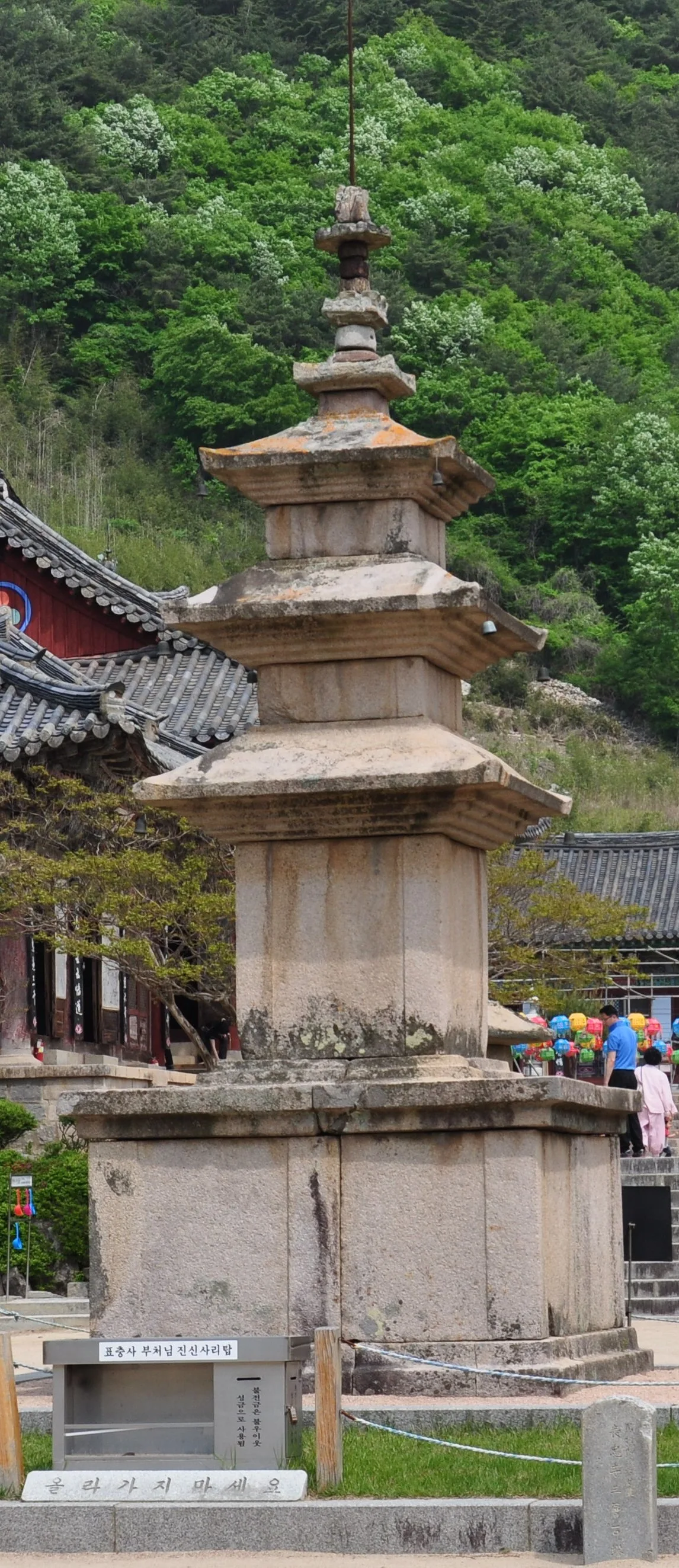 표충사 경내에 세워진 삼층석탑 근접 사진, 뒤로 기와지붕과 신록이 우거진 산이 보인다
