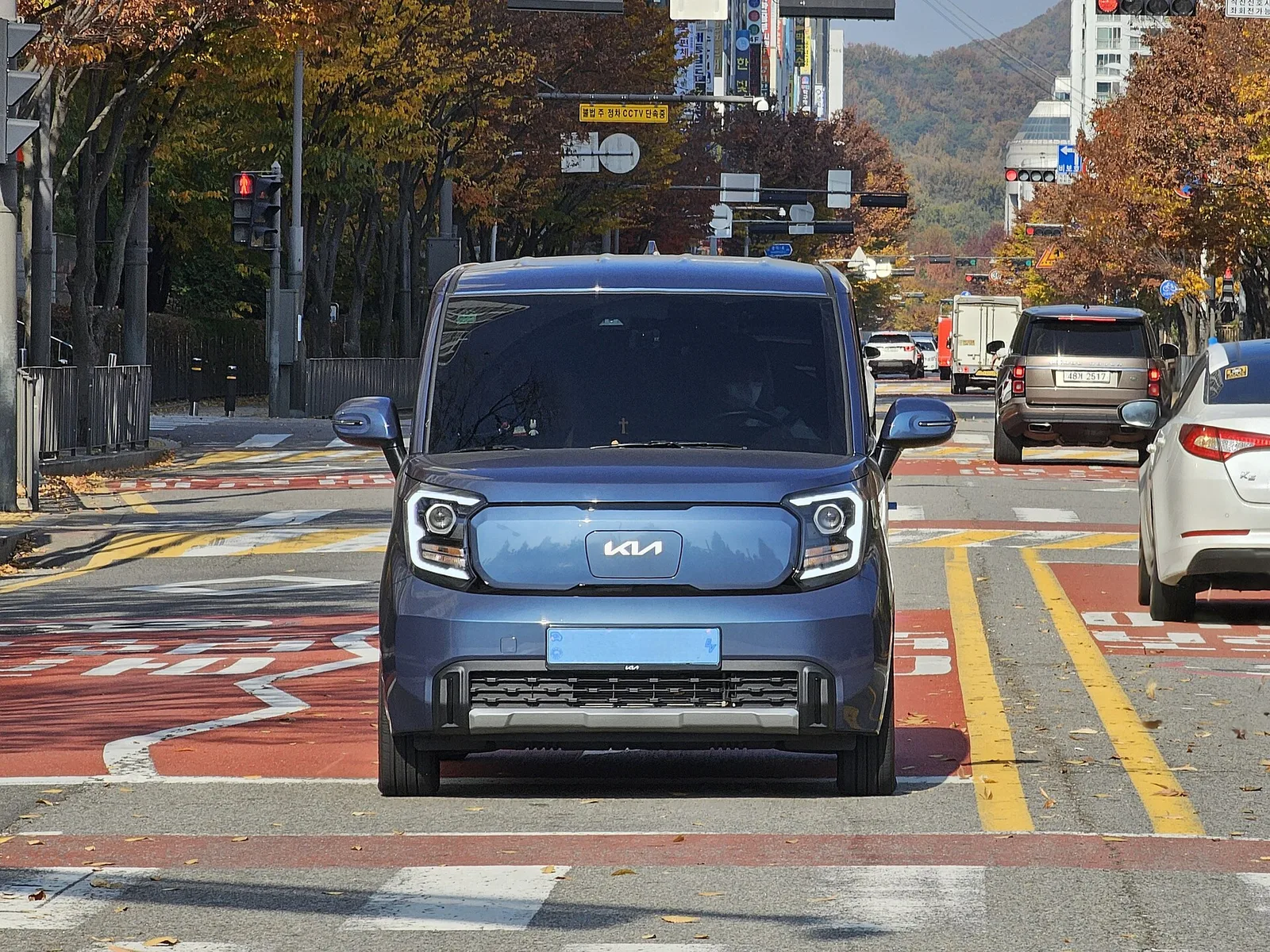 교차로 앞에 서 있는 파란색 계열 기아 레이 EV 정면, 번호판 글자는 보이지 않는다