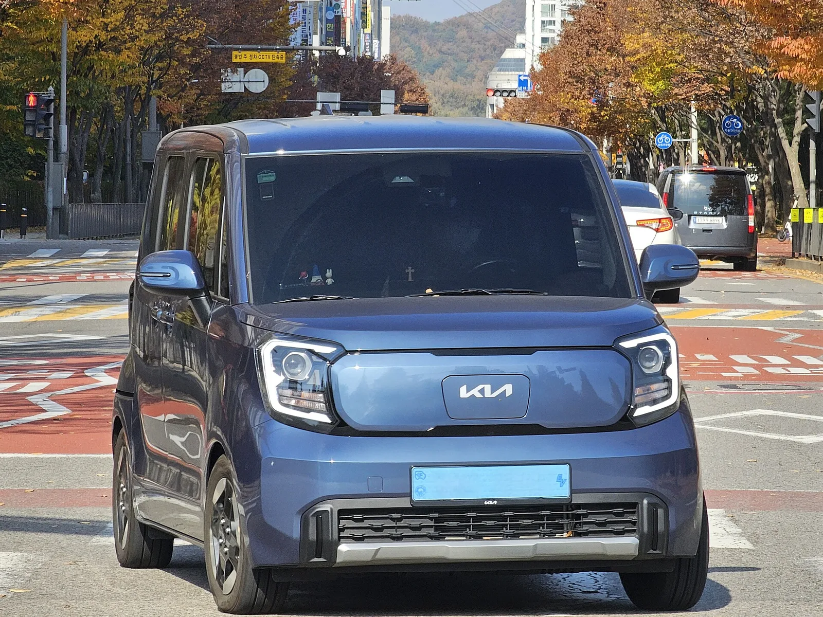 도로 위에서 앞쪽을 향한 파란색 계열 기아 레이 EV 전측면 사진, 번호판 글자는 보이지 않는다