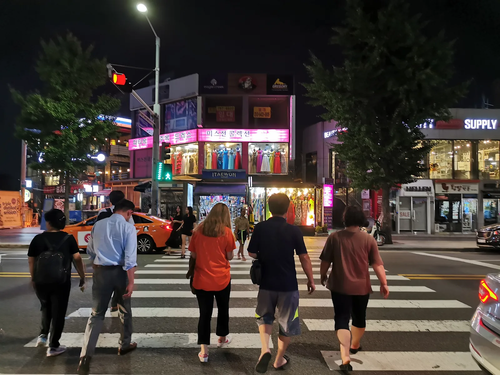 야간에 횡단보도를 건너는 보행자들과 정지 신호등, 대기 중인 차량이 보이는 교차로 모습