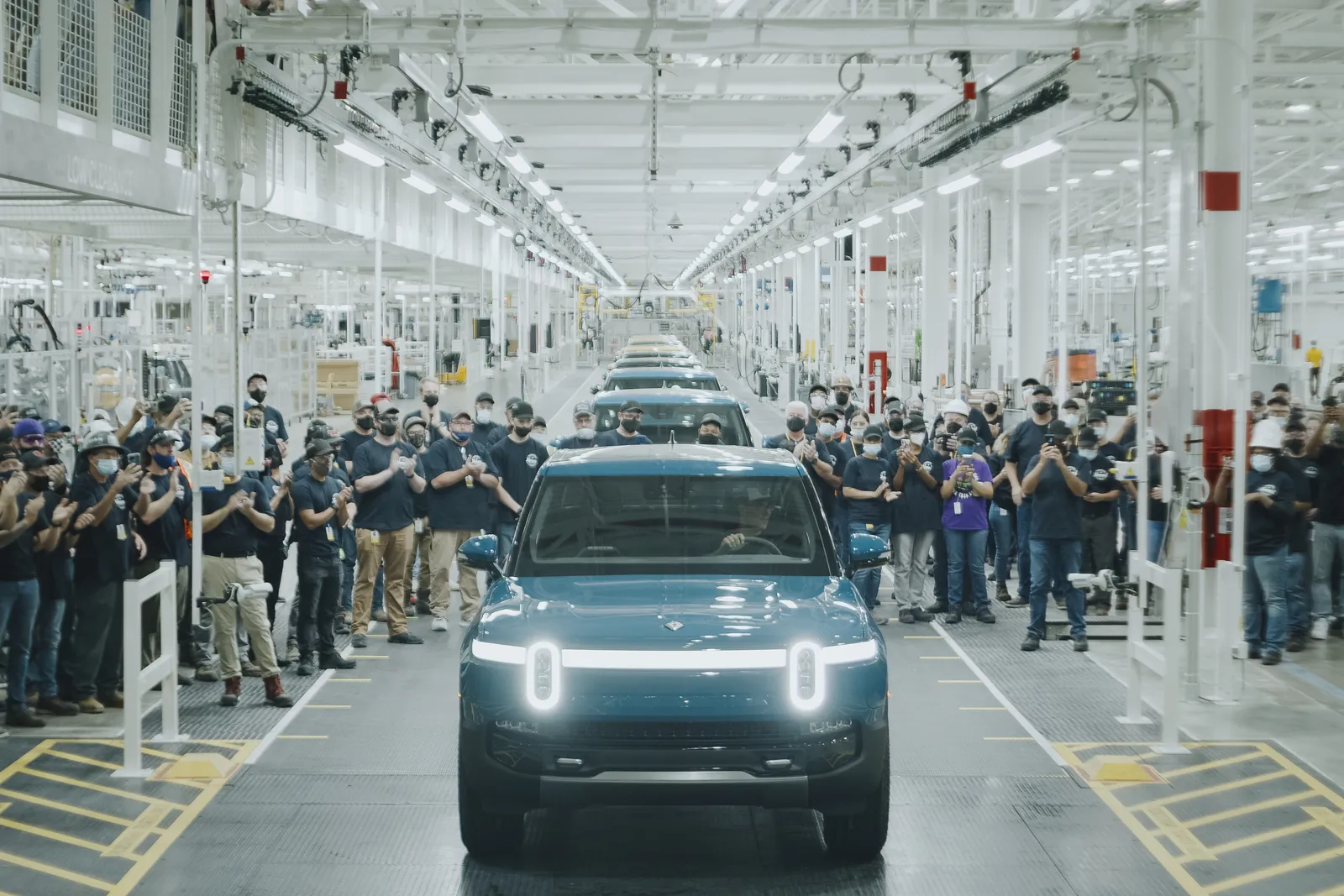 일리노이주 노멀 공장 생산라인에서 직원들의 박수를 받으며 이동하는 짙은 청색 리비안 SUV