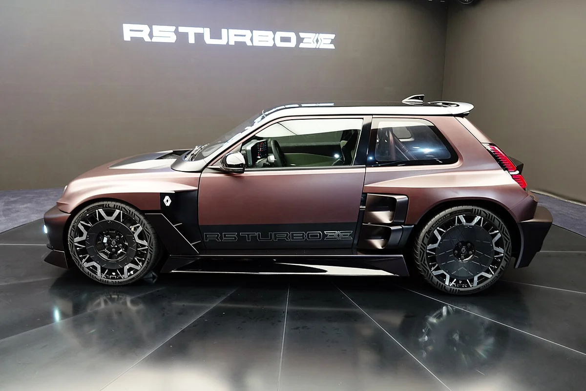 갈색 무광 르노 R5 터보 3E의 측면, 넓은 펜더와 큰 휠이 보이고 뒤쪽 벽에 R5 TURBO 3E 로고가 있다
