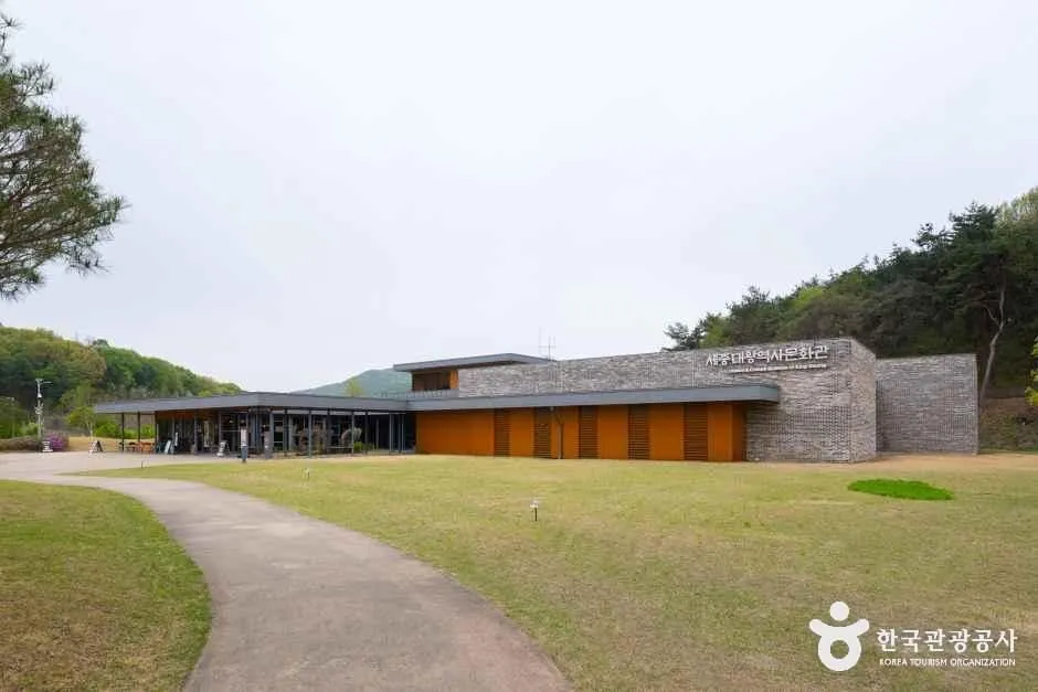 넓은 잔디 광장 옆으로 소나무 숲과 현대식 건물이 보이는 길