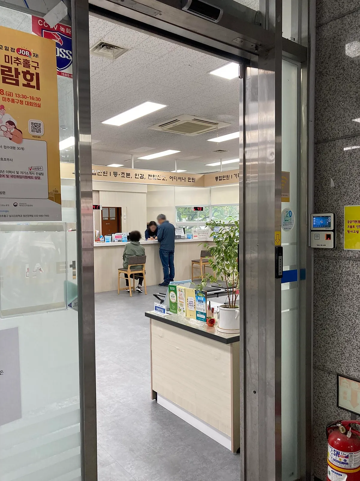 행정복지센터 민원실 입구에서 등초본 인감 전입신고 접수 안내판 아래 민원인이 상담받는 모습
