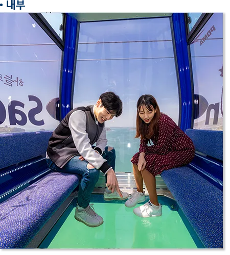 크리스탈 캐빈 내부, 강화유리 투명 바닥 아래로 바다가 비치고 탑승객들이 발아래를 내려다보고 있다