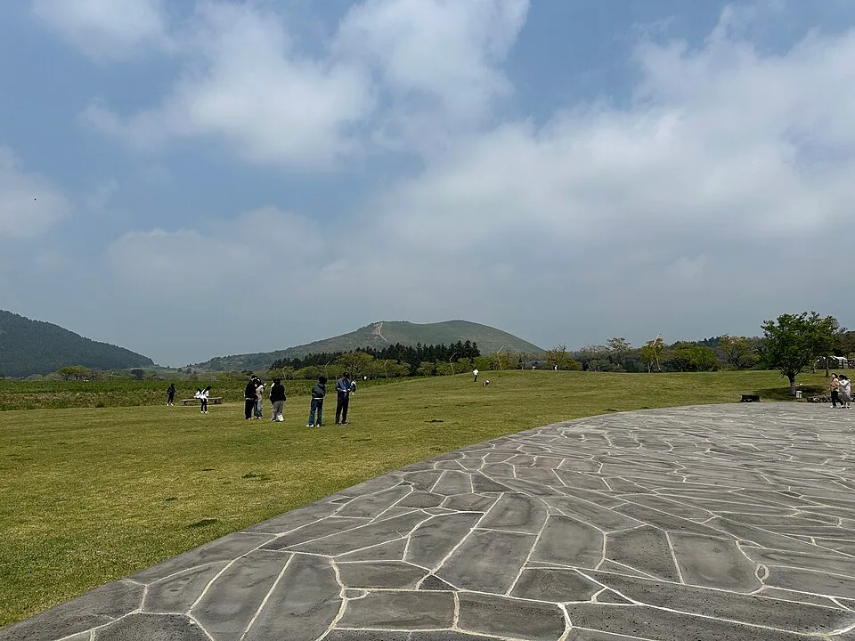 새별오름 입구의 포장된 산책로와 이를 따라 걷는 방문객들, 뒤로 오름 사면이 보인다