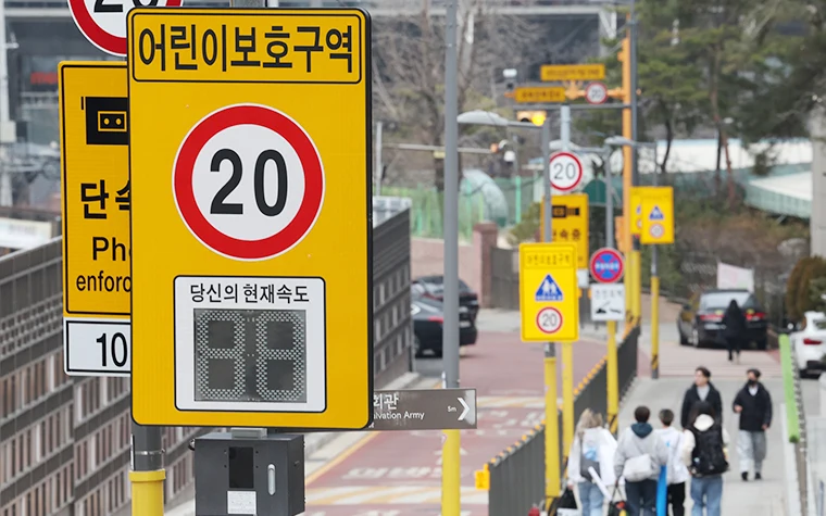어린이보호구역 단속카메라 안내판과 실시간 속도 표시 전광판, 20km 제한속도 표지판이 설치된 거리 모습