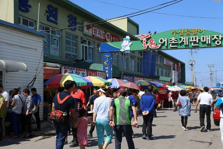 홍원항 어촌계판매장 앞 거리에 사람들이 붐비는 축제 기간 모습, 알록달록한 파라솔이 늘어서 있다