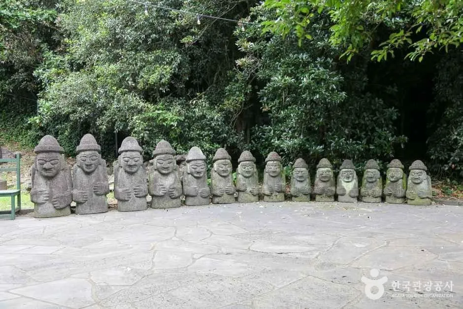 숲을 배경으로 돌하르방 여러 기가 일렬로 서 있는 모습