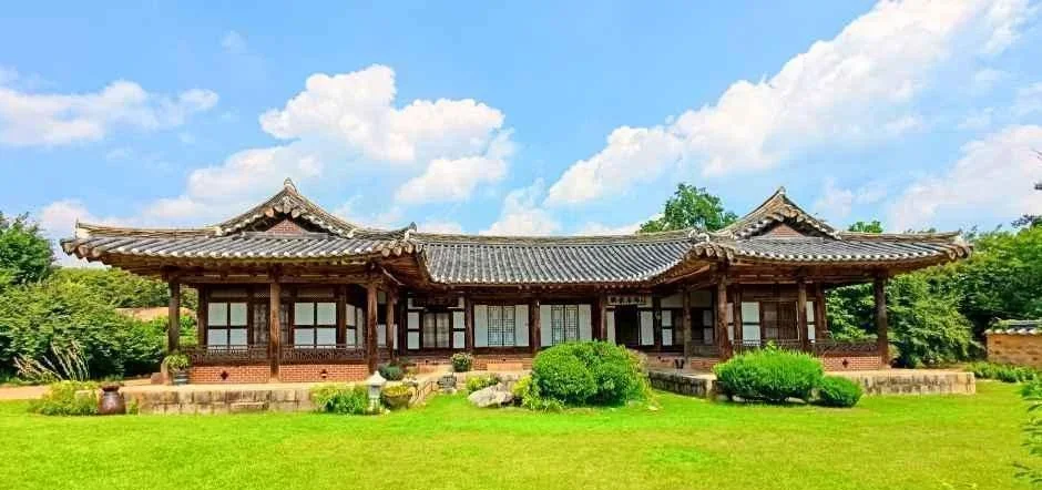 푸른 하늘 아래 잔디 마당 너머로 보이는 안채