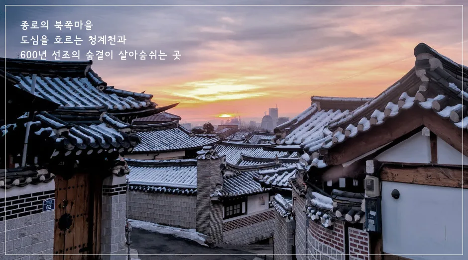 노을이 물든 북촌한옥마을 기와지붕 전경, 뒤로 서울 도심 빌딩이 보인다