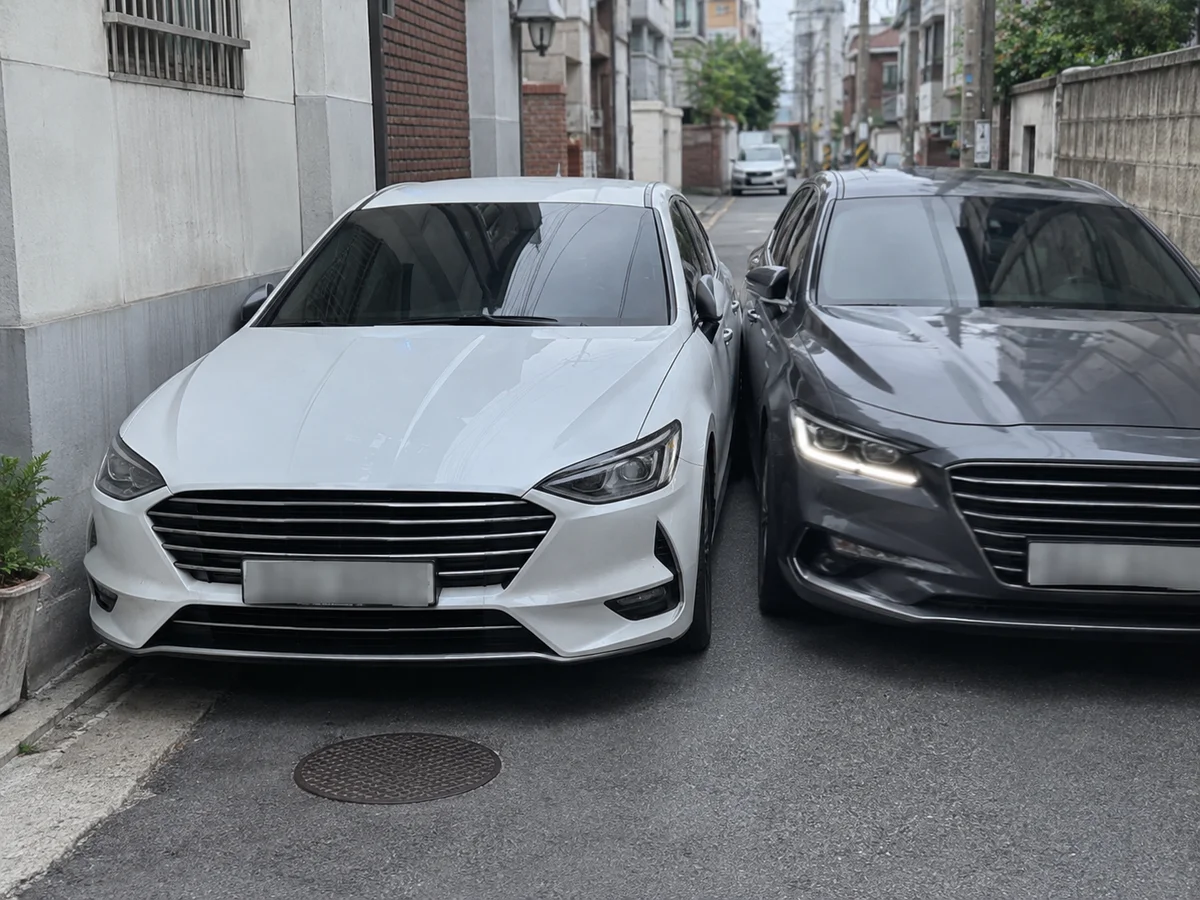 좁은 주택가 골목에 흰색 세단과 짙은 색 세단이 사이드미러를 맞댈 듯 가깝게 주차돼 있는 모습