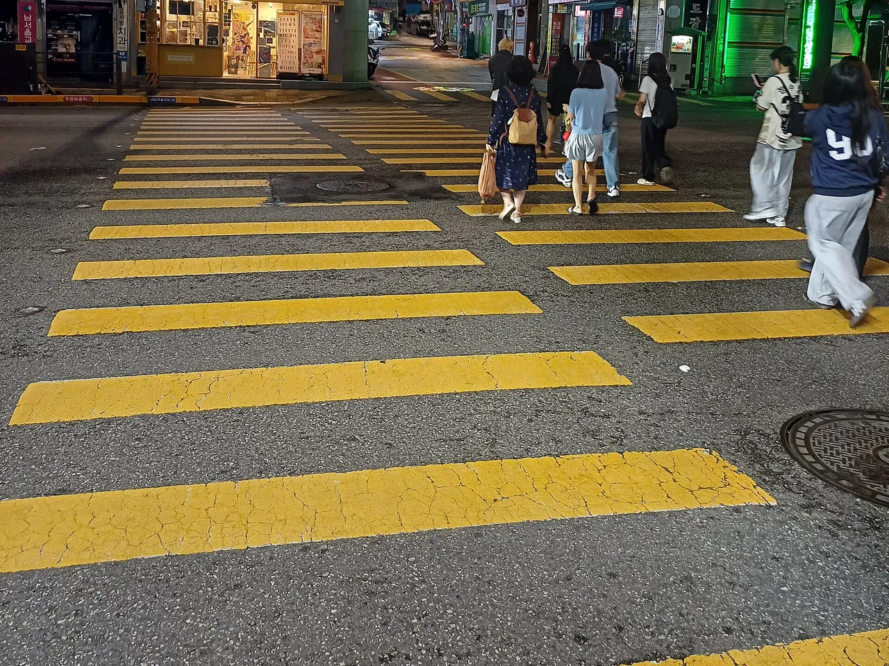 밤 시내 교차로의 노란색으로 칠한 횡단보도와 건너는 보행자들
