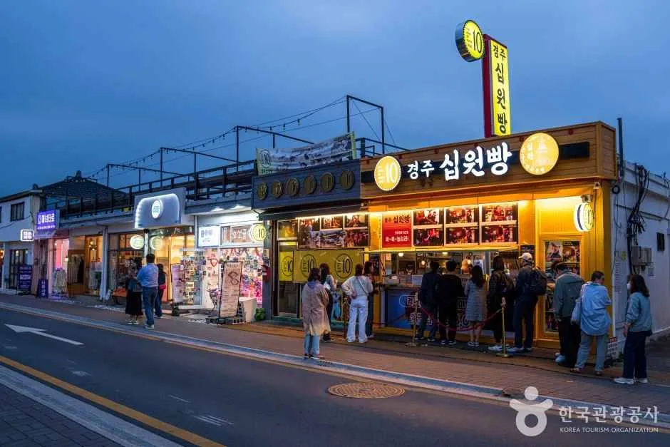 저녁 무렵 가게 간판 불빛이 켜진 거리에서 사람들이 줄을 서 있는 황리단길의 모습