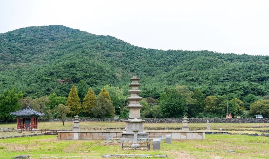 녹색 산자락 아래 넓은 잔디 절터와 석탑, 붉은 전각이 보이는 성주사지 전경