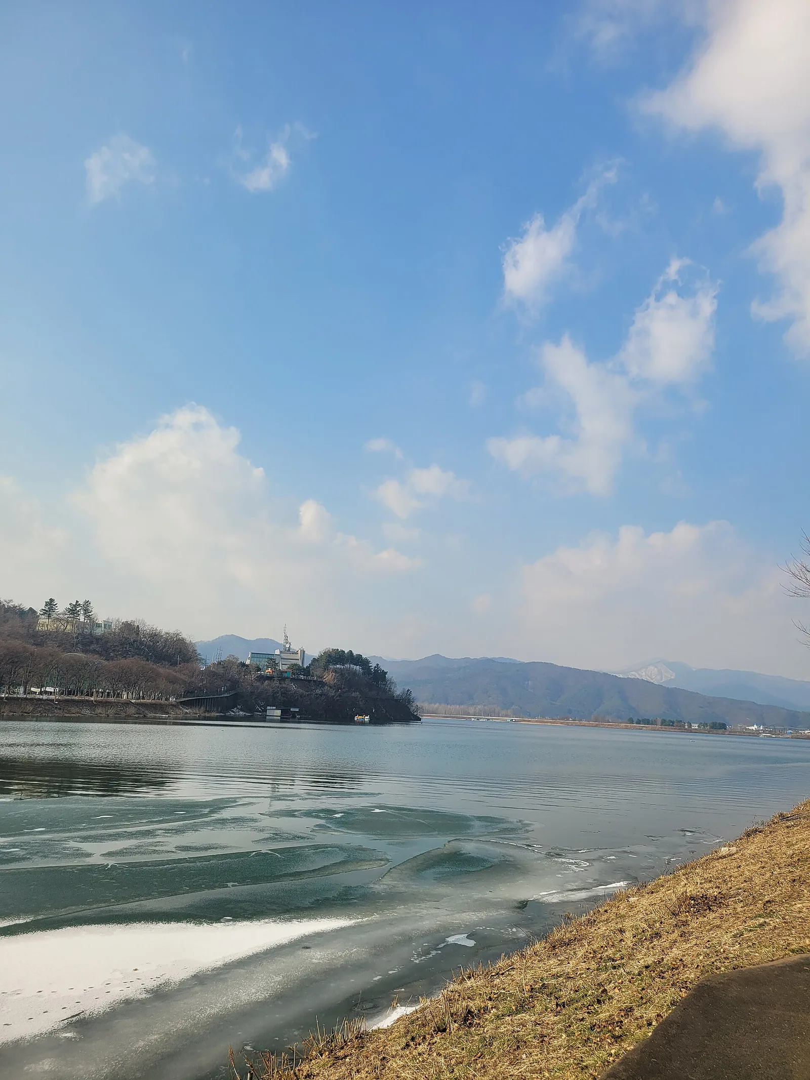 공지천유원지에서 바라본 의암호 전경, 잔잔한 호수와 건너편 산줄기, 작은 섬 전망대가 보인다