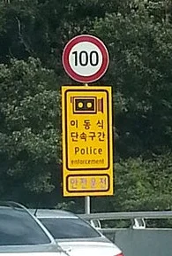 노란 바탕에 카메라 그림과 이동식 단속구간, Police enforcement, 안전운전 문구가 적힌 안내 표지와 그 위의 제한속도 표지
