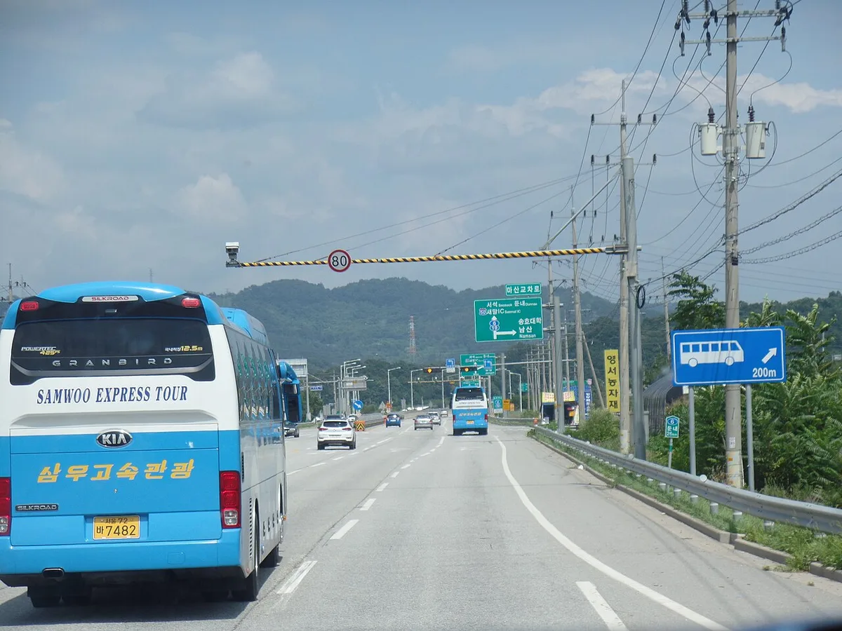국도에서 상단 구조물에 제한속도 표지와 단속 장비가 설치돼 있고 버스가 주행하는 모습