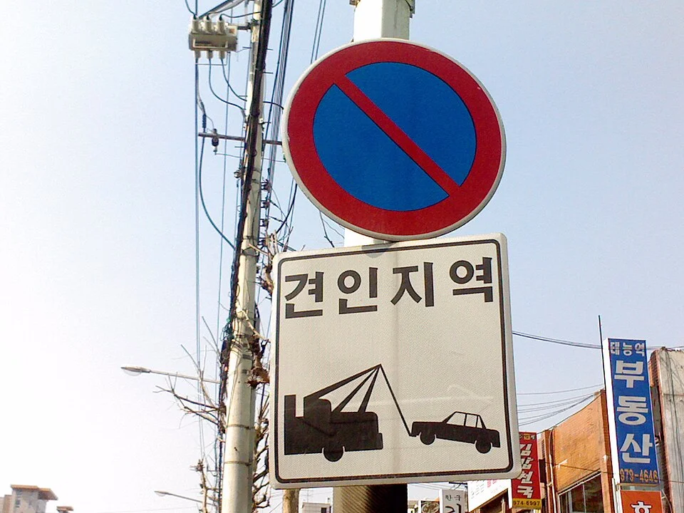 파란 원판에 붉은 사선이 그려진 주차금지 표지와 견인지역 보조표지