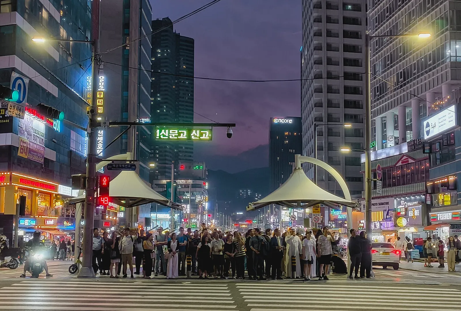 해운대 구남로 문화광장 횡단보도 앞에서 황혼 무렵 신호를 기다리는 많은 보행자와 점등된 간판들