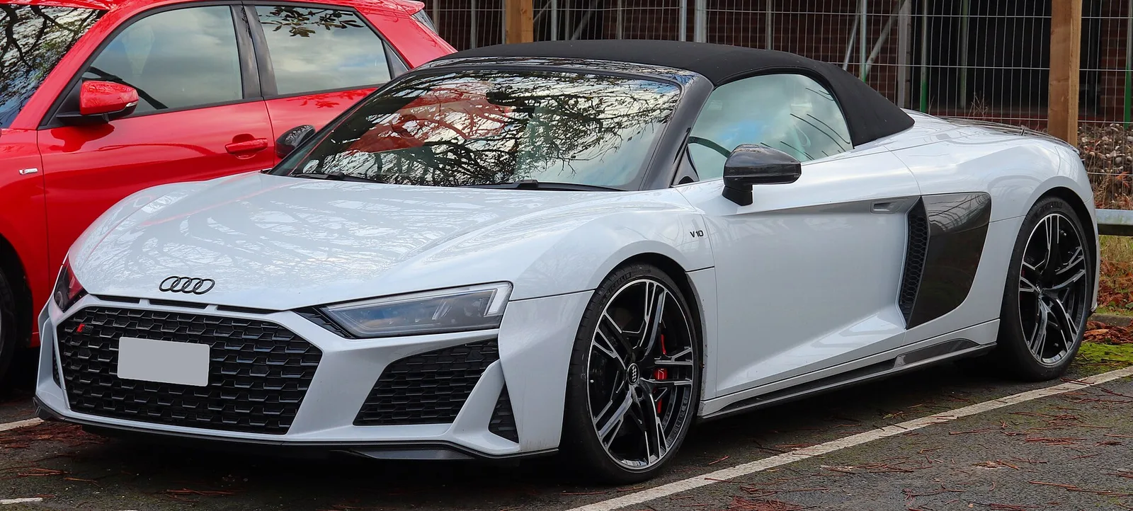 흰색 아우디 R8 V10 스파이더가 소프트톱을 닫은 채 주차된 정면 측면 모습, 문에 V10 배지가 보임