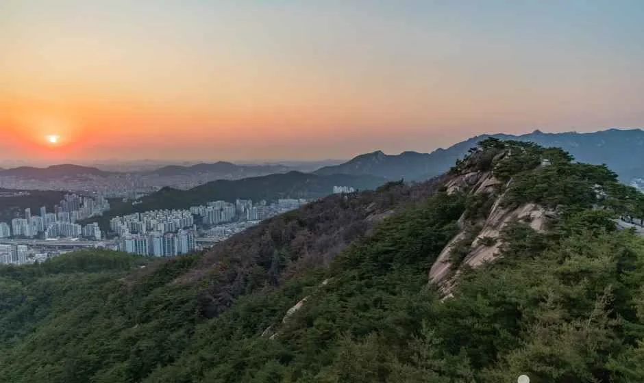 붉은 노을 아래 암릉이 솟은 산 능선과 도심 건물이 보이는 인왕산 일대
