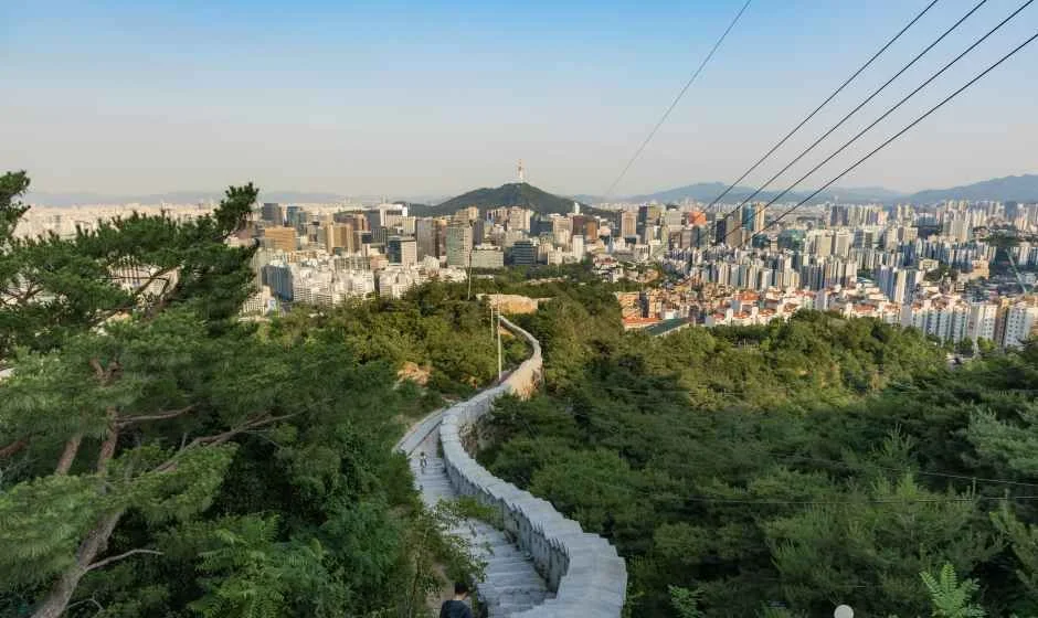 돌로 쌓은 성곽 길이 산 능선을 따라 이어지고 멀리 도심 건물이 보이는 인왕산 한양도성