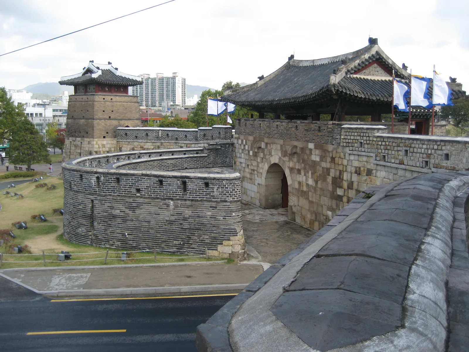 수원화성 성곽 둘레길과 공심돈, 성문이 보이는 낮 전경, 뒤로 수원 시내 아파트 단지가 보인다