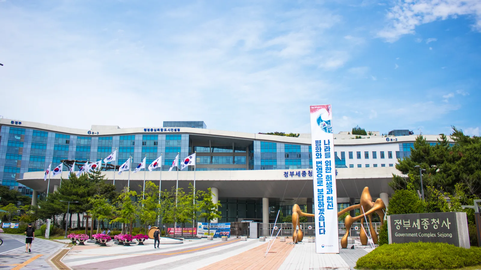 태극기가 늘어선 정부세종청사 정문 전경, '정부세종청사'라는 표지판이 보인다