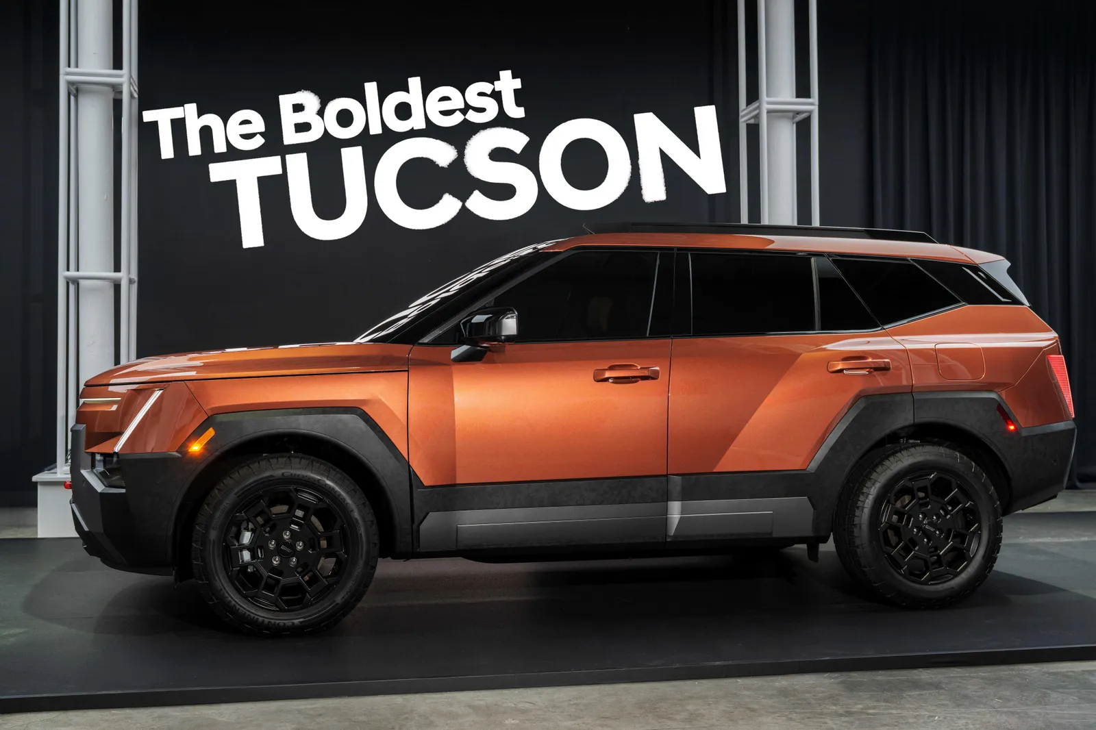 The Boldest TUCSON 문구가 걸린 행사 무대에 전시된 오렌지색 현대 신형 투싼의 측면