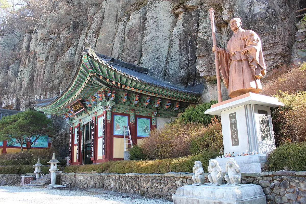 바위 절벽 아래 단청 법당과 석상이 서 있는 사찰 경내
