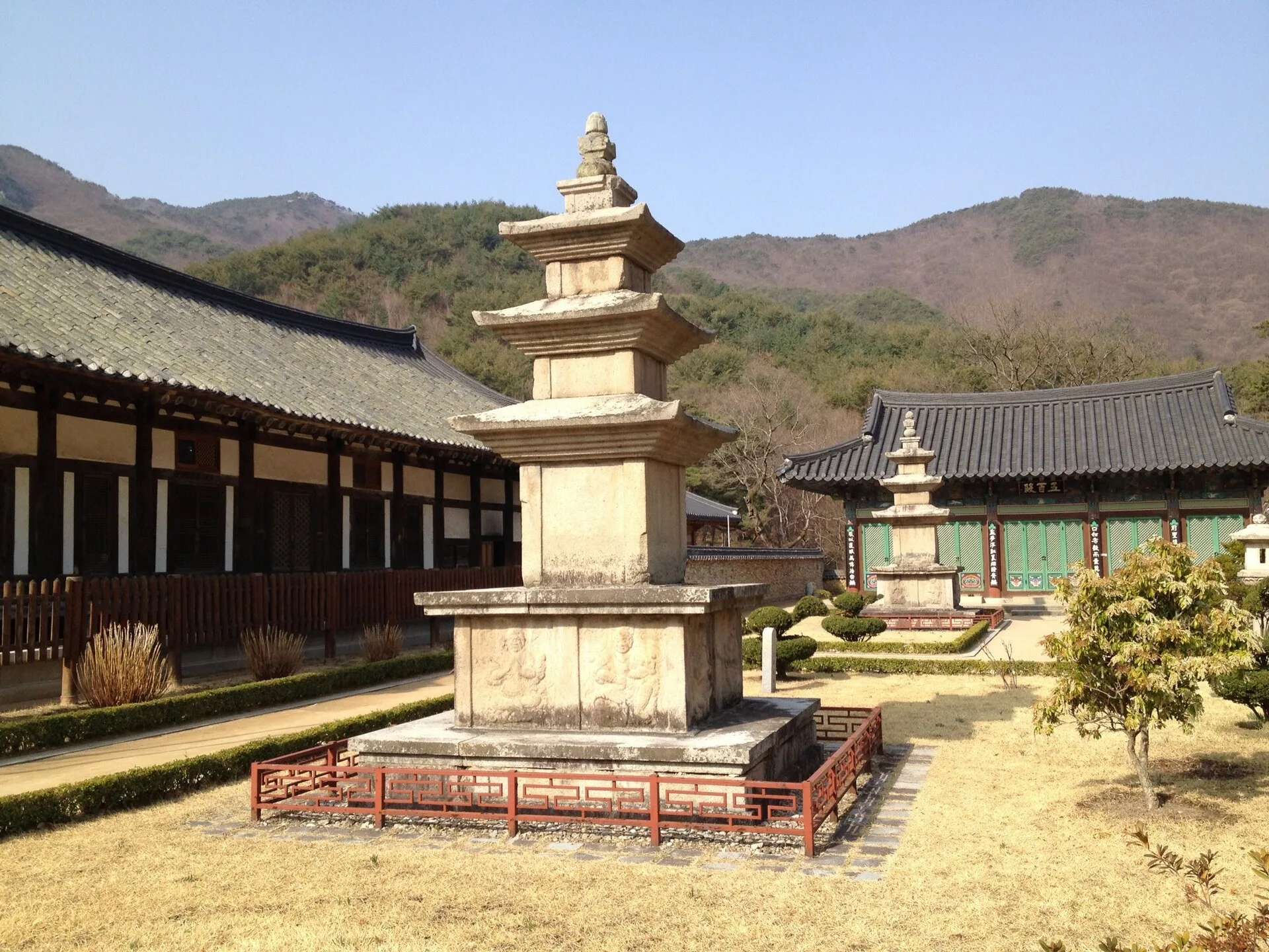 전각 옆 잔디밭에 서 있는 삼층석탑과 뒤쪽 산