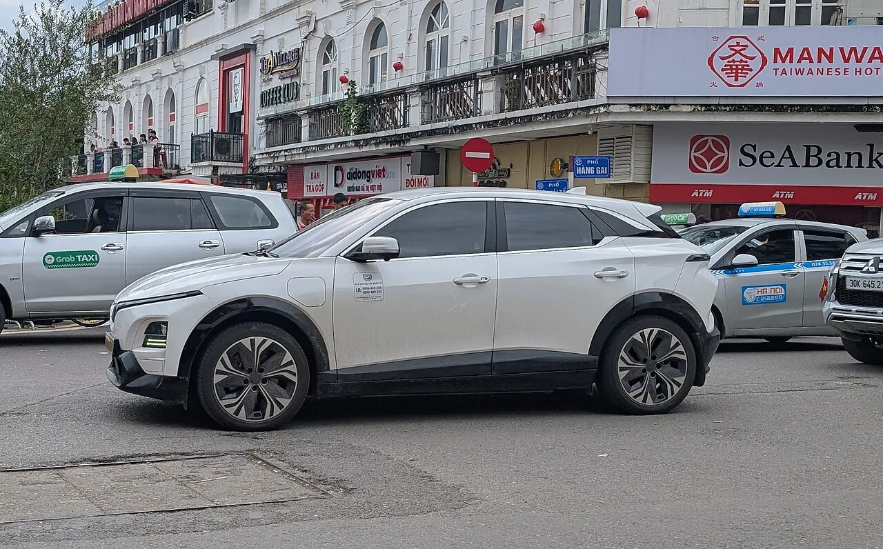 베트남 하노이 시내 교차로에서 그랩 택시들 사이를 지나는 흰색 빈패스트 VF6 SUV