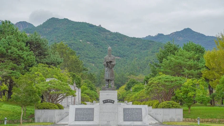 산자락을 배경으로 기단 위에 세워진 왕인박사 동상