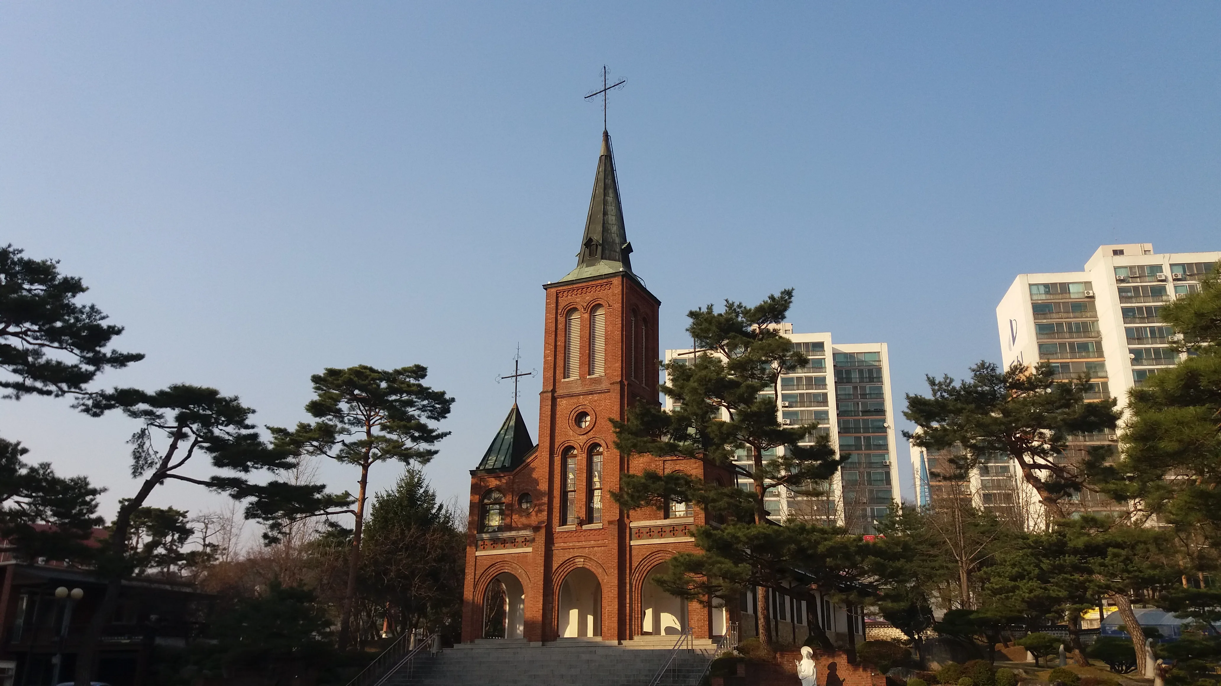 안성성당 종탑, 붉은 벽돌로 지은 고딕 양식 종탑과 십자가, 주변을 소나무가 둘러싼 모습