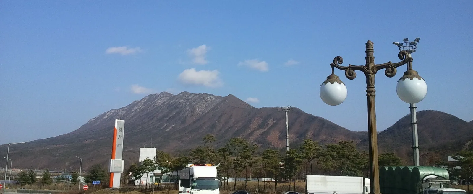 맑은 하늘 아래 바위 능선이 드러난 산을 배경으로 황간 표지탑과 가로등, 트럭이 서 있는 휴게소 주차장