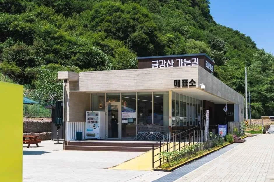 금강산 가는길 매표소 간판이 붙은 단층 건물과 앞쪽 자판기가 보이는 풍경