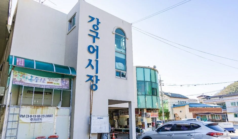 강구어시장 글자가 쓰인 흰색 건물과 주차된 차
